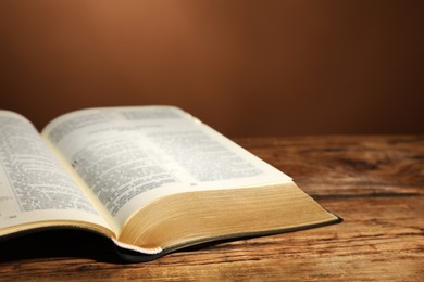 Photo of Open Bible on wooden table against brown background, closeup. Christian religious book
