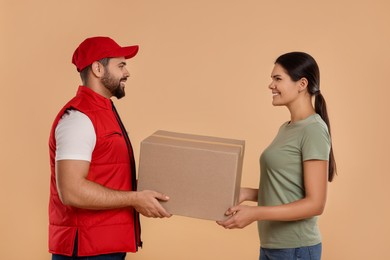 Smiling courier giving parcel to receiver on light brown background