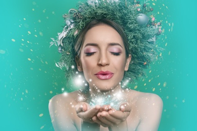 Beautiful young woman with Christmas wreath blowing kiss on color background