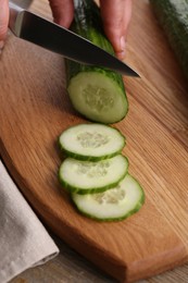 Photo of Woman cutting cucumber on wooden board at table, closeup