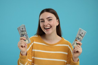 Happy woman with dollar banknotes on light blue background