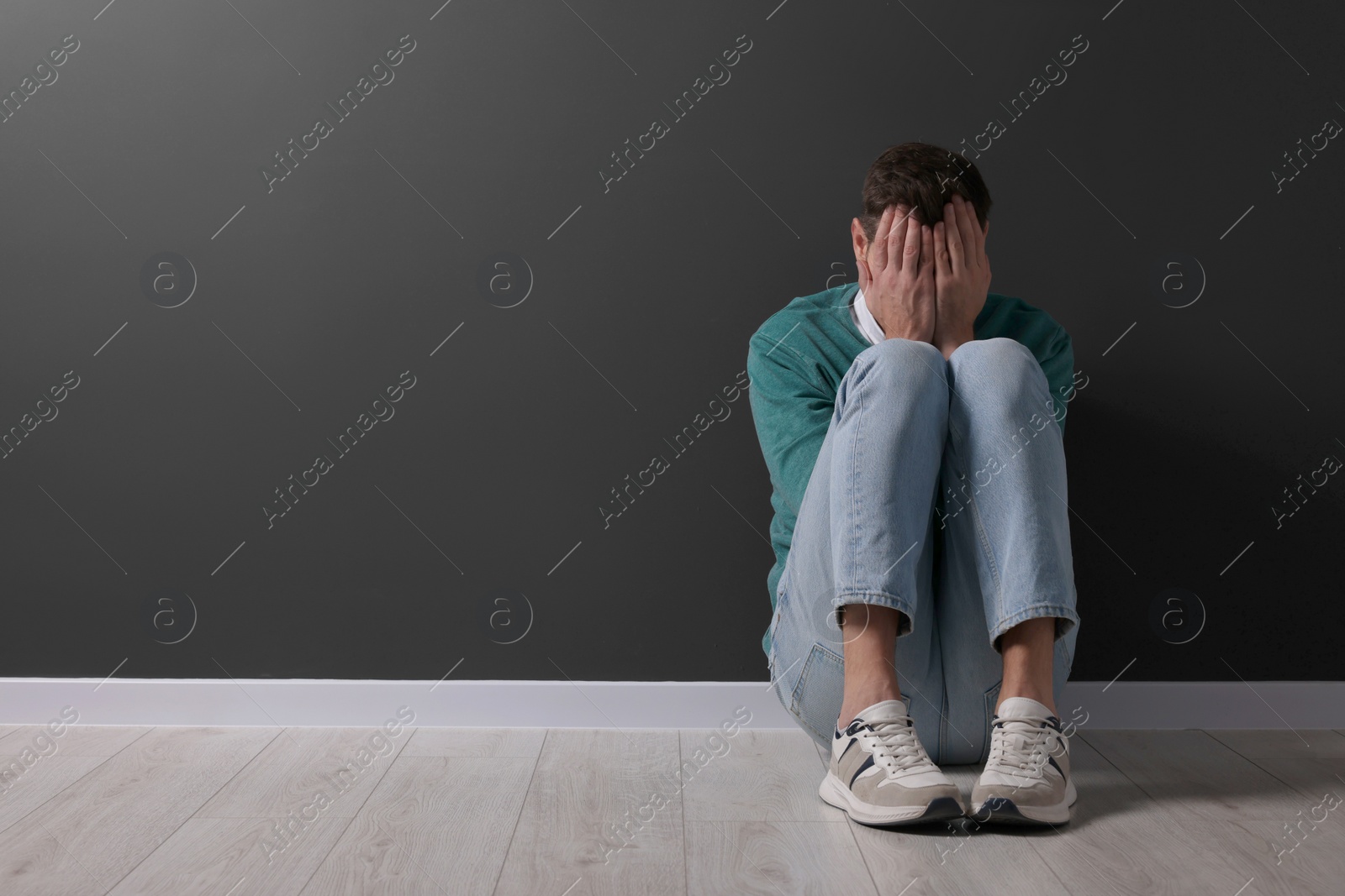 Photo of Upset man sitting on floor near black wall. Space for text