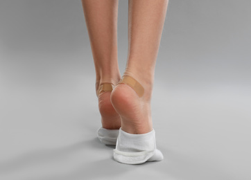 Photo of Girl showing feet with sticking plasters on light grey background, closeup