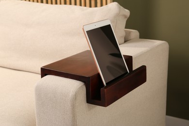 Photo of Tablet on sofa armrest wooden table in room. Interior element