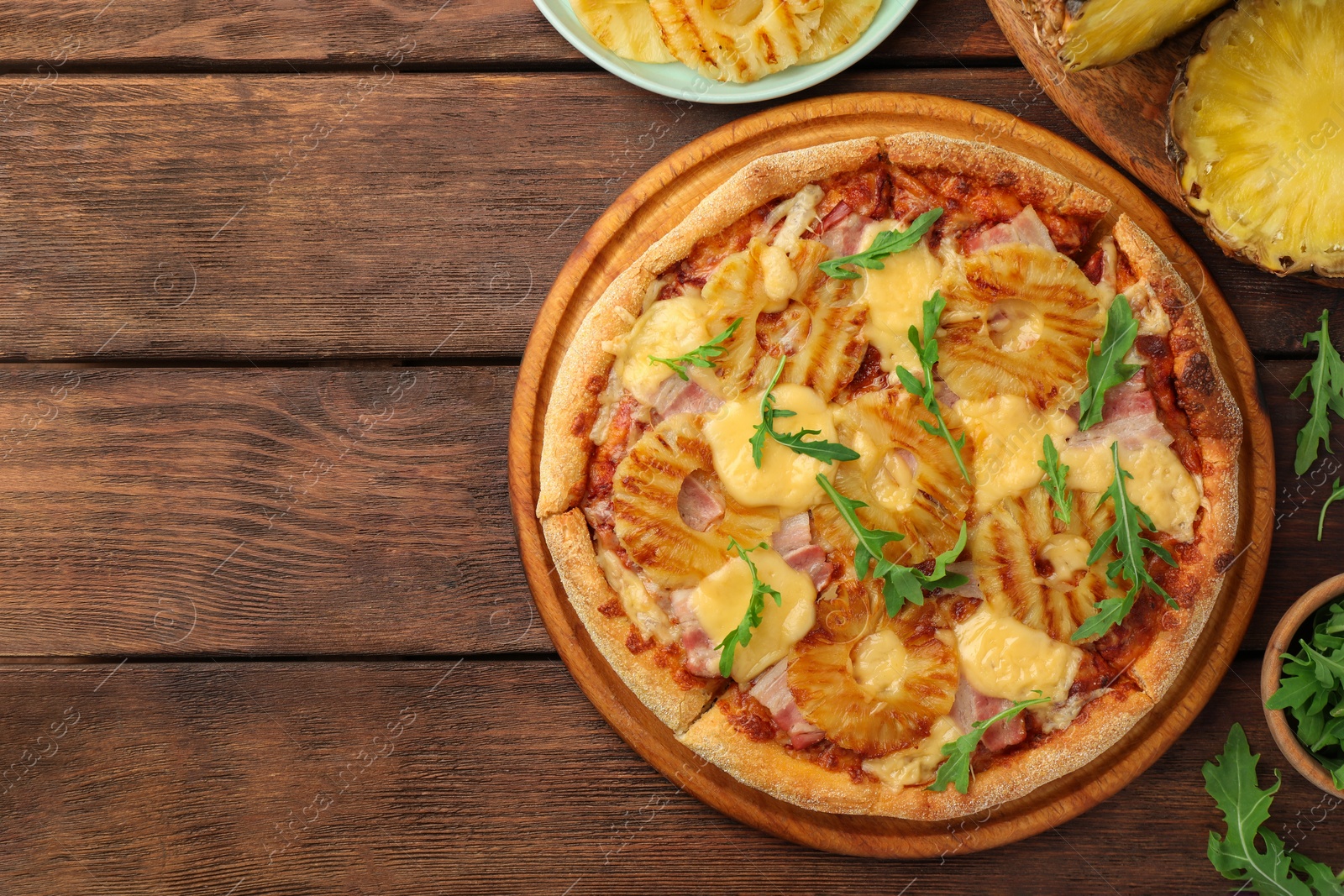 Photo of Delicious pineapple pizza and ingredients on wooden table, flat lay. Space for text