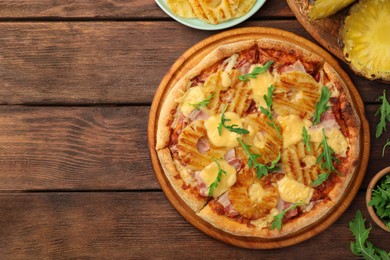 Photo of Delicious pineapple pizza and ingredients on wooden table, flat lay. Space for text