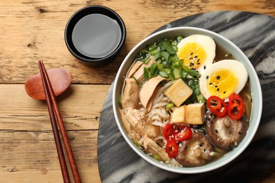 Noodle soup. Bowl of delicious ramen and chopsticks on wooden table, flat lay