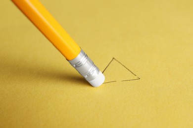 Erasing triangle with graphite pencil on yellow background, closeup