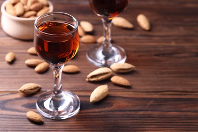 Photo of Liqueur glass with tasty amaretto and almonds on wooden table, closeup. Space for text