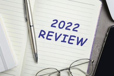 Image of Text 2022 Review written in notebook, pen and glasses on grey table, top view