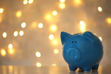 Photo of Piggy bank on wooden table against blurred Christmas lights, space for text