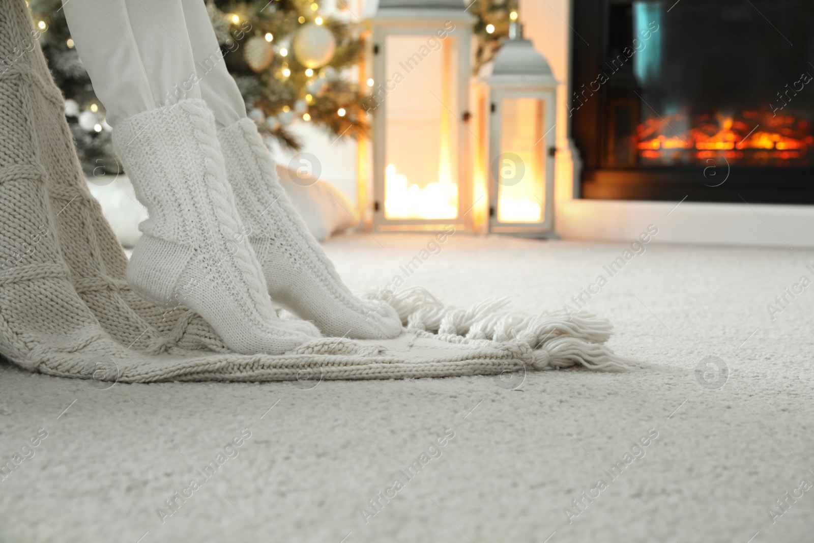 Photo of Woman in knitted socks resting near fireplace at home, closeup