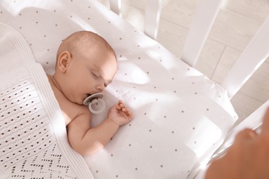 Photo of Cute little baby with pacifier sleeping in crib, above view. Space for text