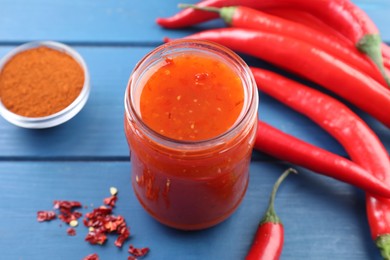 Photo of Spicy chili sauce in jar and ingredients on blue wooden table, closeup