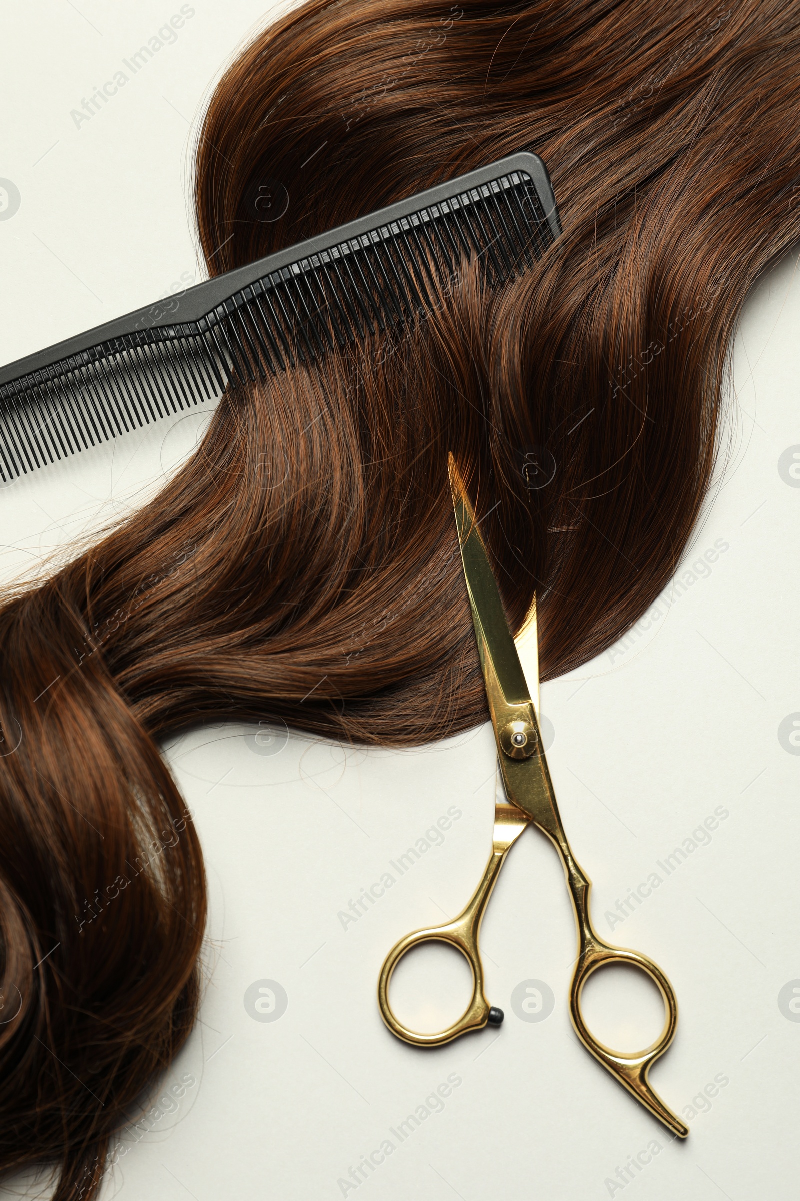 Photo of Professional hairdresser scissors and comb with brown hair strand on light grey background, flat lay