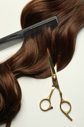 Professional hairdresser scissors and comb with brown hair strand on light grey background, flat lay