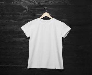 Hanger with stylish white T-shirt on black wooden wall