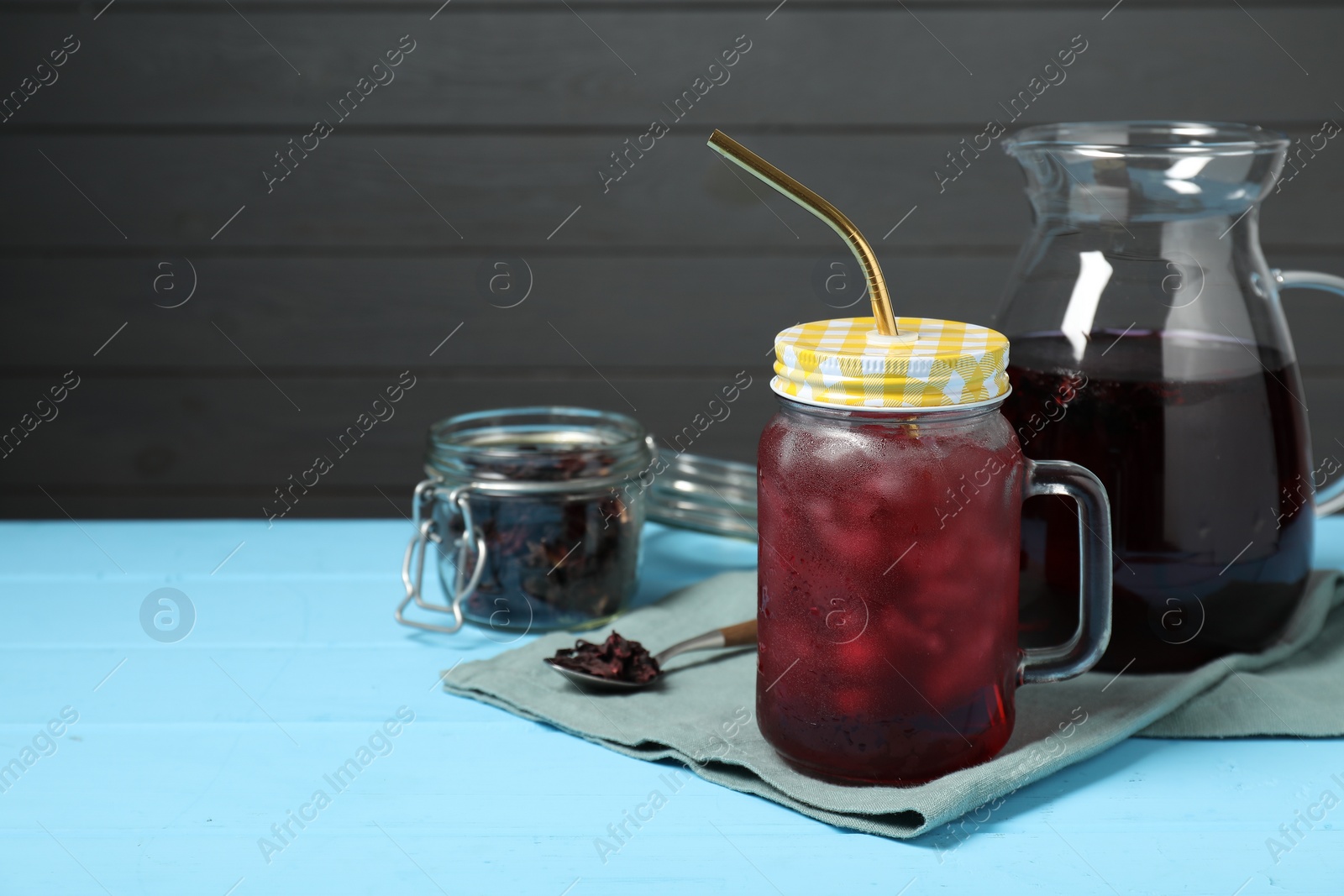 Photo of Delicious iced hibiscus tea and dry flowers on light blue wooden table, space for text