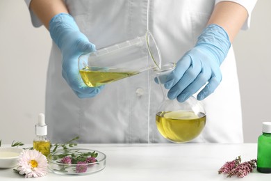 Scientist developing cosmetic oil at white table, closeup