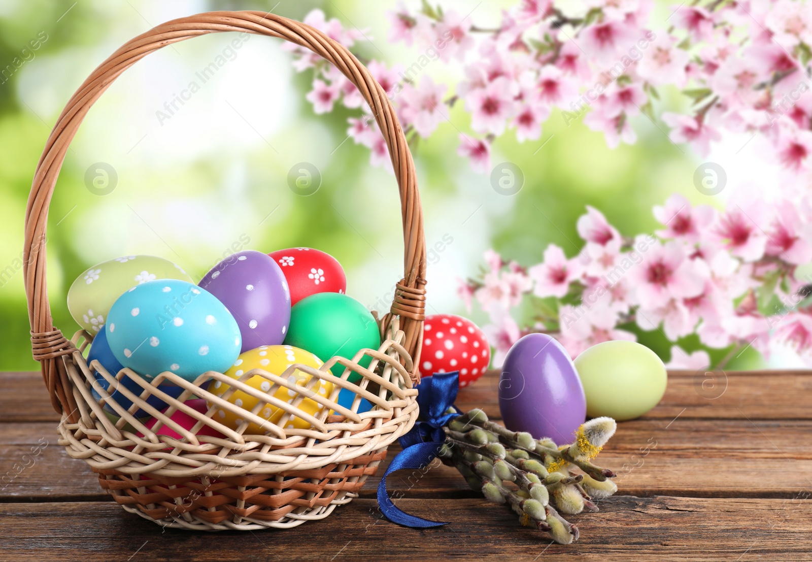 Image of Colorful Easter eggs in wicker basket on wooden table outdoors 