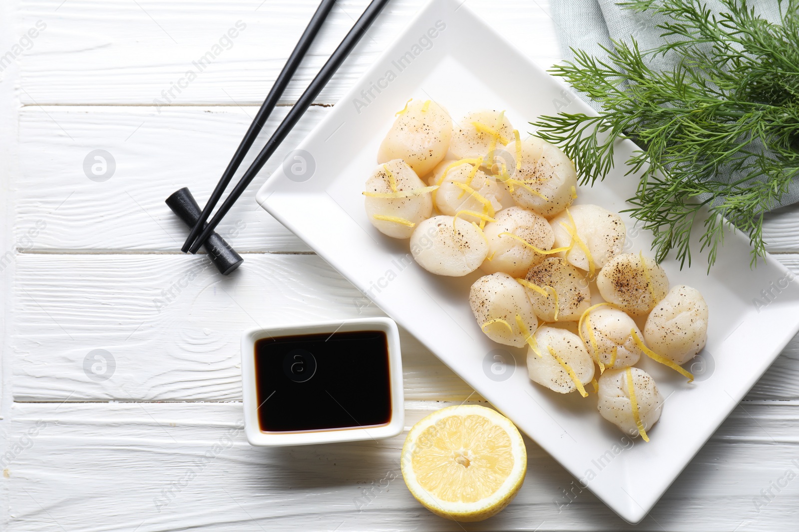 Photo of Raw scallops with milled pepper, lemon zest, dill and soy sauce on white wooden table, flat lay