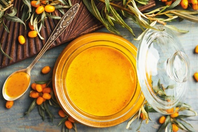 Photo of Delicious sea buckthorn jam and fresh berries on blue wooden table, flat lay