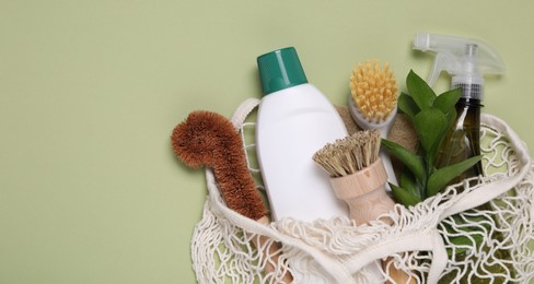 Different cleaning supplies in string bag on green background, space for text