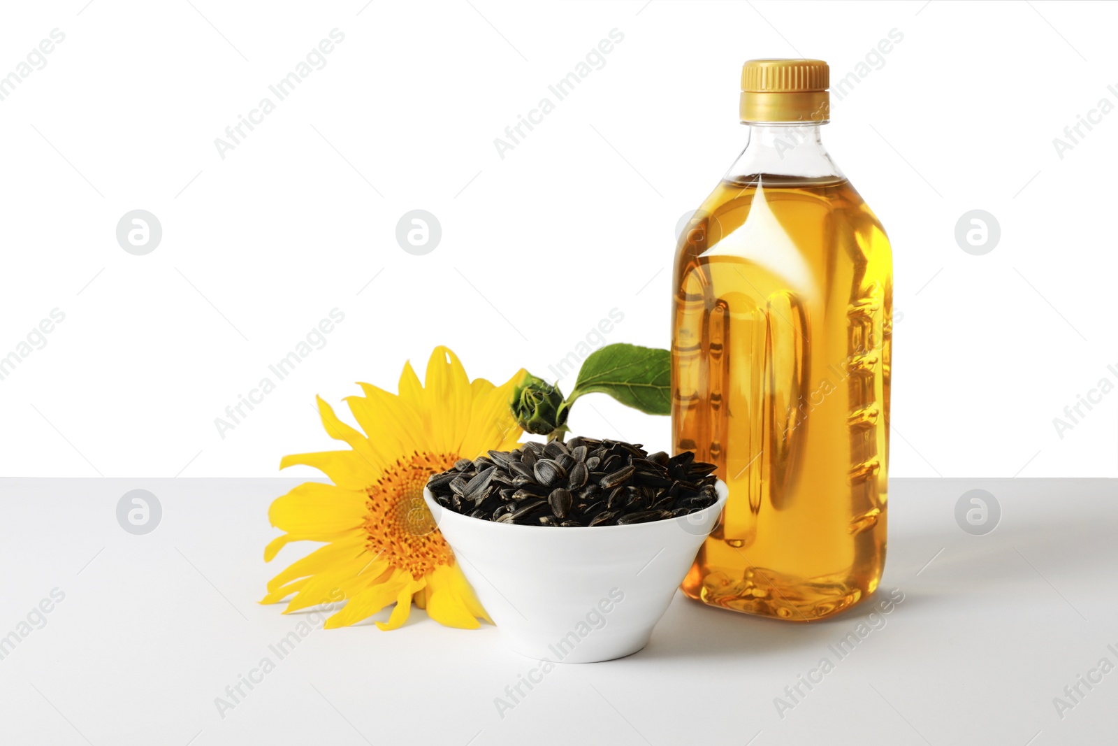 Photo of Bottle of cooking oil, sunflower seeds and flower on white background