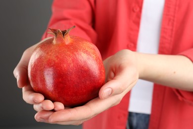 Photo of Woman holding whole pomegranate on grey background, closeup