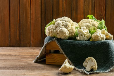 Photo of Crate with cut and whole cauliflowers on wooden table. Space for text