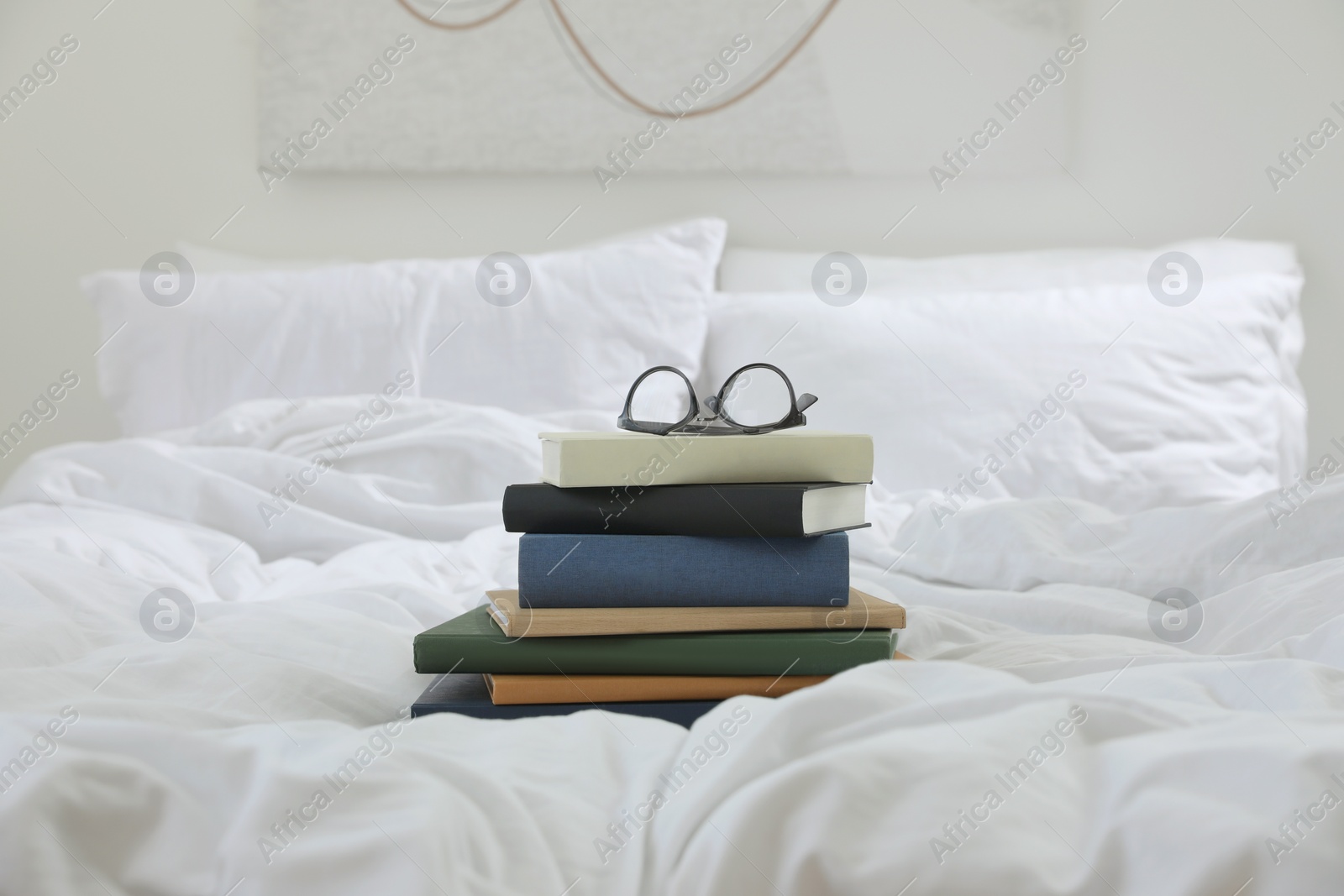 Photo of Hardcover books and glasses on bed indoors