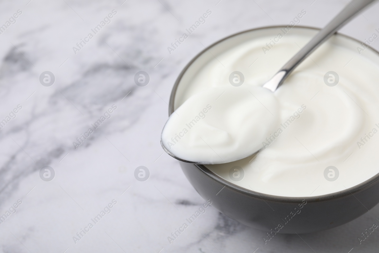 Photo of Delicious natural yogurt in bowl and spoon on white marble table, closeup. Space for text