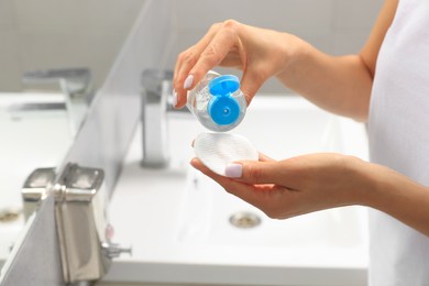 Photo of Woman pouring micellar water onto cotton pad in bathroom, closeup