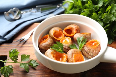 Delicious cooked snails with parsley in bowl on table, closeup