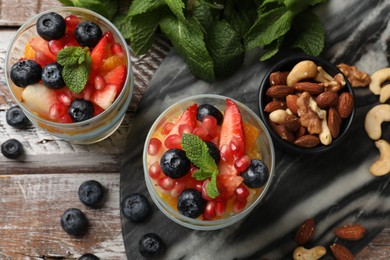 Photo of Delicious fruit salad, fresh berries, mint and nuts on wooden table, flat lay