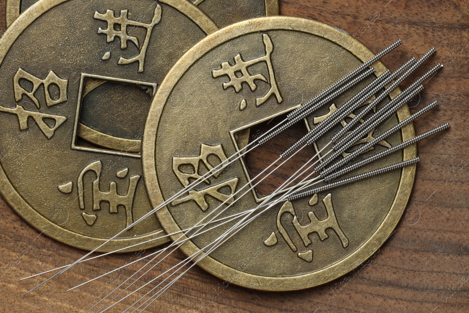 Photo of Acupuncture needles and Chinese coins on wooden table, flat lay