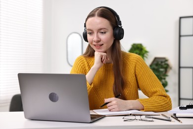 E-learning. Young woman using laptop during online lesson at white table indoors