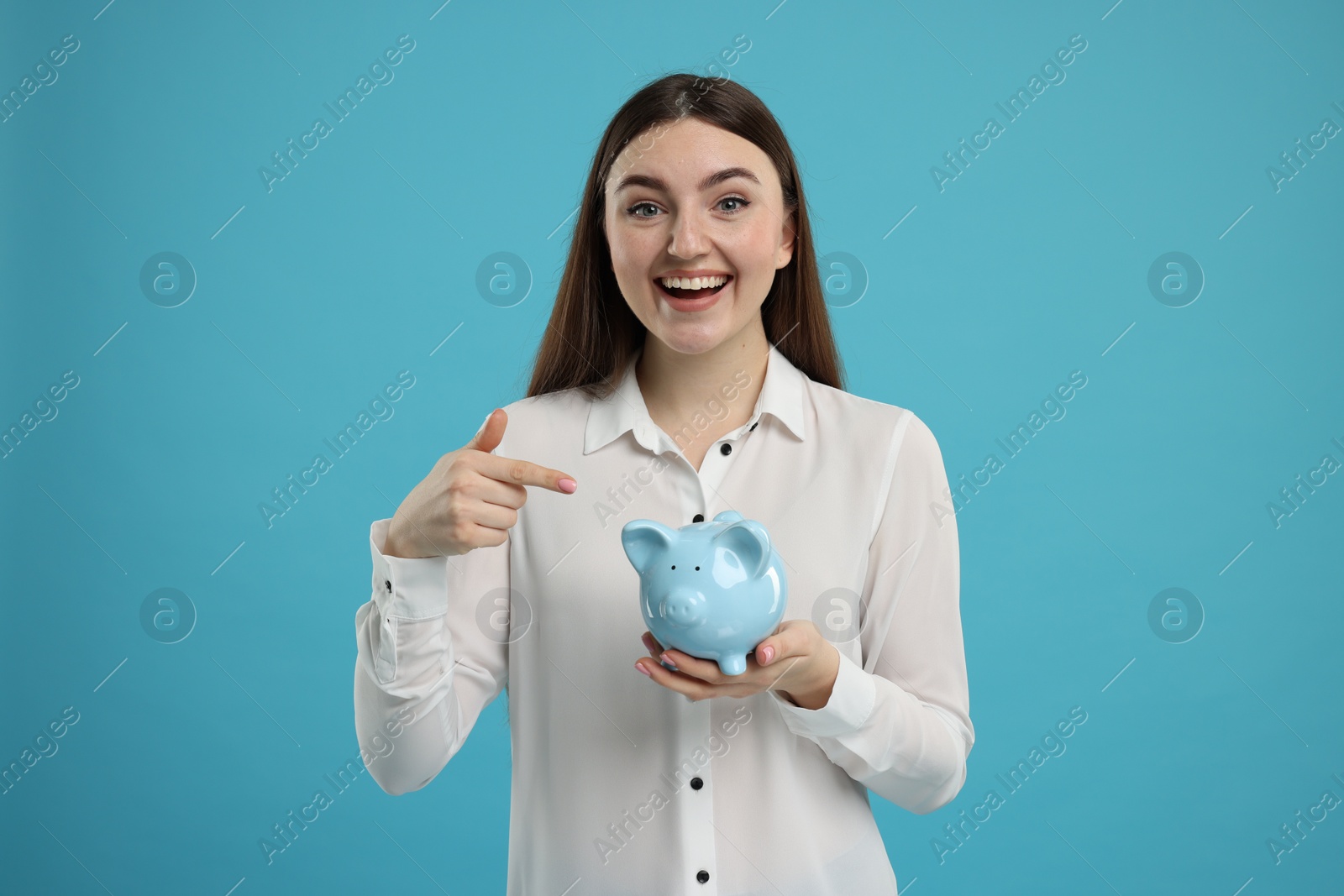 Photo of Excited woman pointing at piggy bank on light blue background