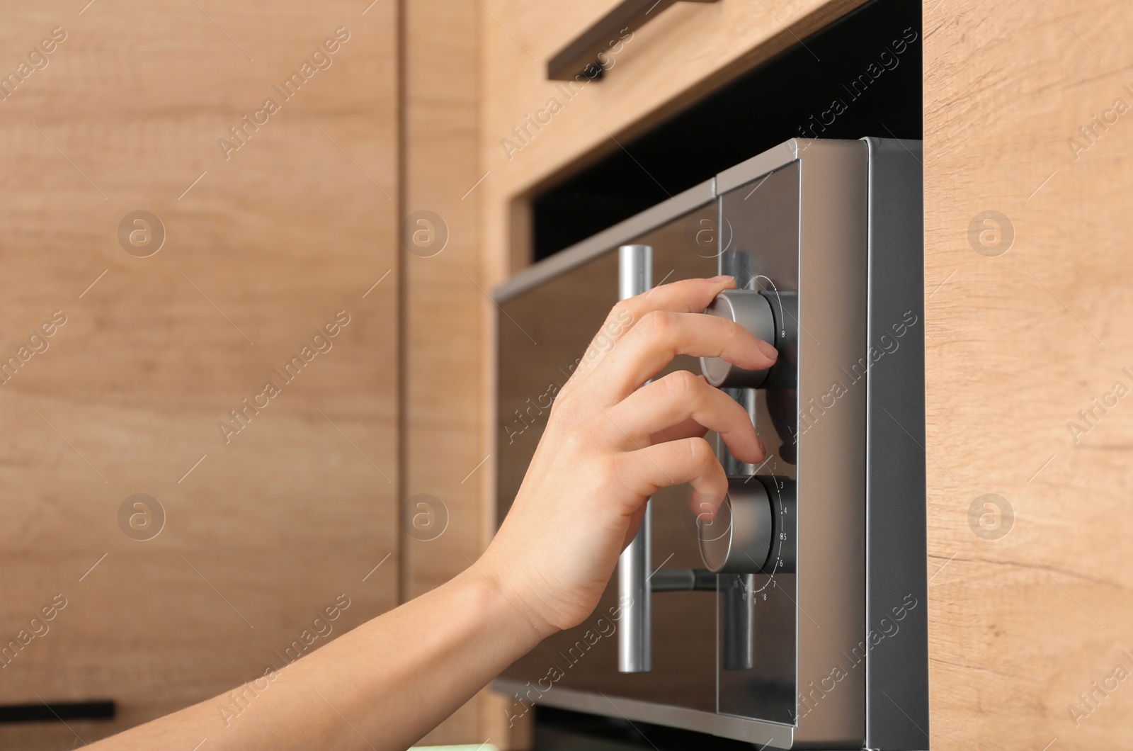 Photo of Young woman adjusting modern microwave oven in kitchen, closeup