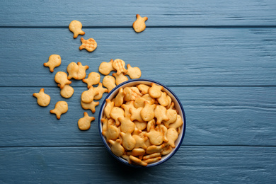 Photo of Delicious goldfish crackers in bowl on blue wooden table, flat lay
