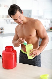Photo of Young shirtless athletic man preparing protein shake in kitchen