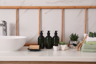 Photo of Soap dispensers, towels and plants on countertop in bathroom
