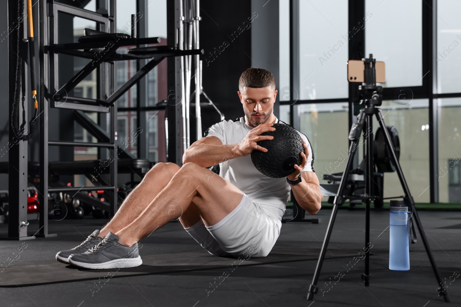 Photo of Man with ball streaming online training on phone at gym. Fitness coach