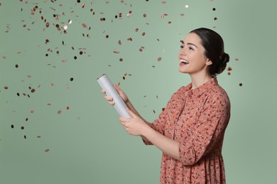 Young woman blowing up party popper on pale green background