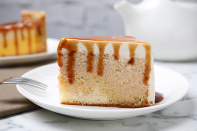 Photo of Slice of delicious cake with caramel sauce on white marble table