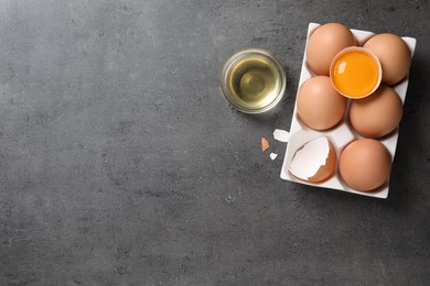 Box of whole and cracked chicken eggs on grey table, flat lay. Space for text