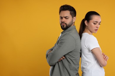Resentful couple with crossed arms on orange background, space for text