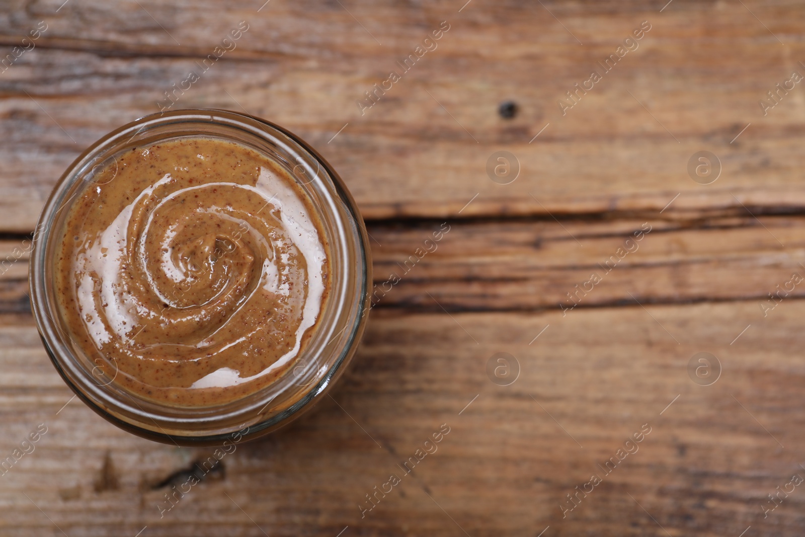 Photo of Tasty nut paste in jar on wooden table, top view. Space for text