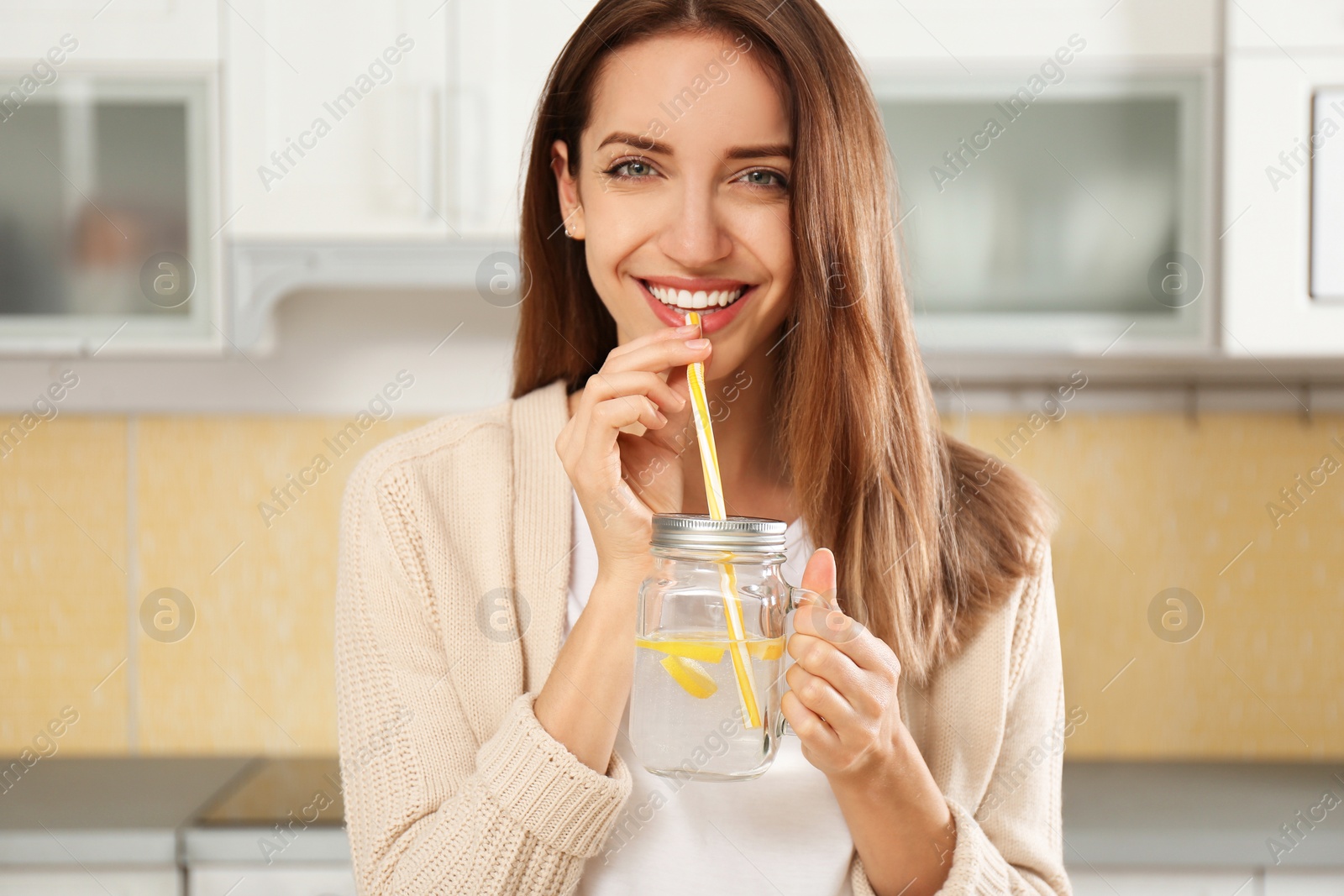 Photo of Young woman drinking lemon water in kitchen