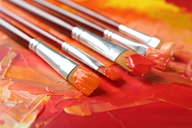 Photo of Set of different brushes on abstract colorful paint, closeup